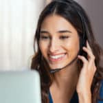Smiling woman using laptop while talking to customer on phone. C